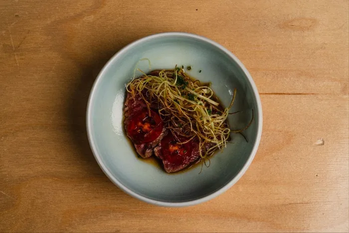 A5 wagyu crudo with nikiri soy, sliced tomatoes, crispy leeks and chives